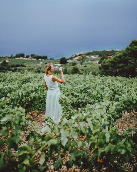 A woman in a field of green plants, holding a glass. 5