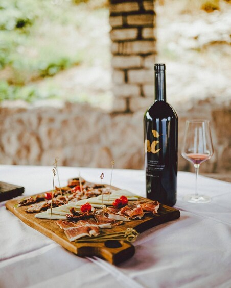 A wooden board with various meats and cheeses, a bottle of wine, and a wine glass on a table. 4