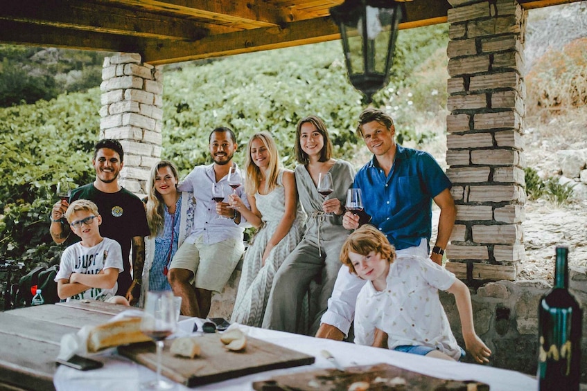 A group of people seated at an outdoor table with food and drinks, under a wooden pergola with stone pillars. 2