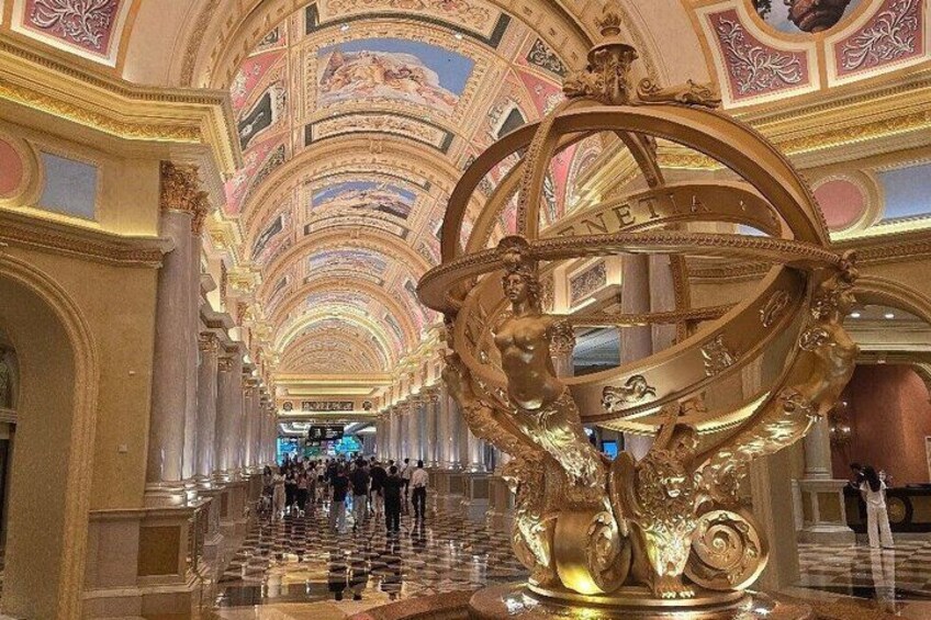 A grand hall with a large golden astronomical sculpture, columns, and a marble floor. 4
