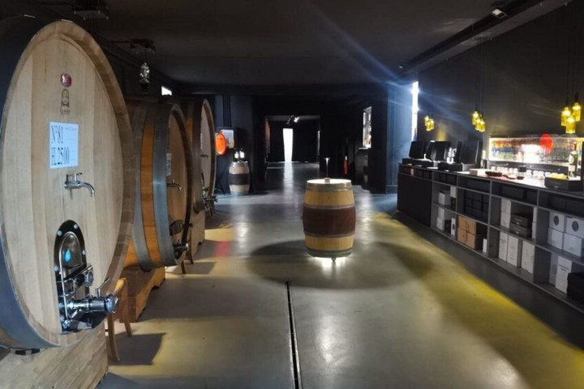 A wine cellar with wooden barrels, a central barrel, and a bar area with hanging lights. 2