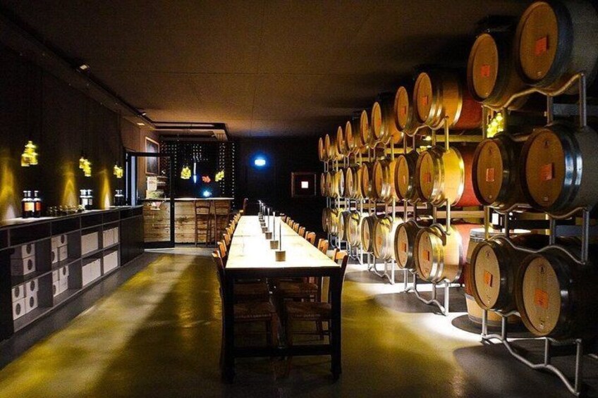 A long table in a dimly lit room with rows of wine barrels on the right. 4