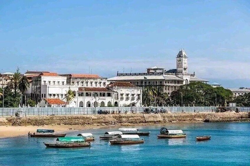 A coastal town with historic buildings, a lighthouse, and several boats on the water. 1