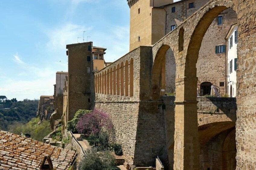 A historic stone wall with arches, a tower, and buildings in the background. 3