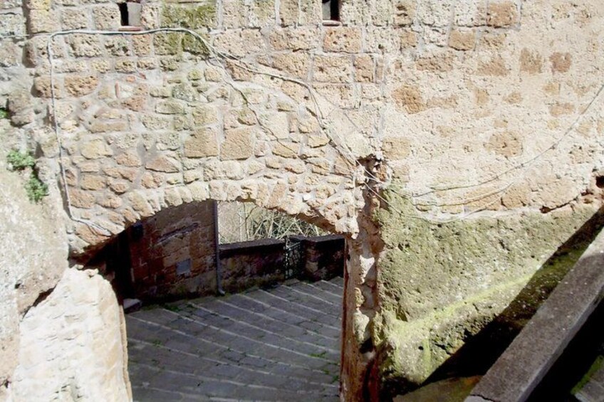 A stone wall with a narrow passageway and a wooden bridge. 2