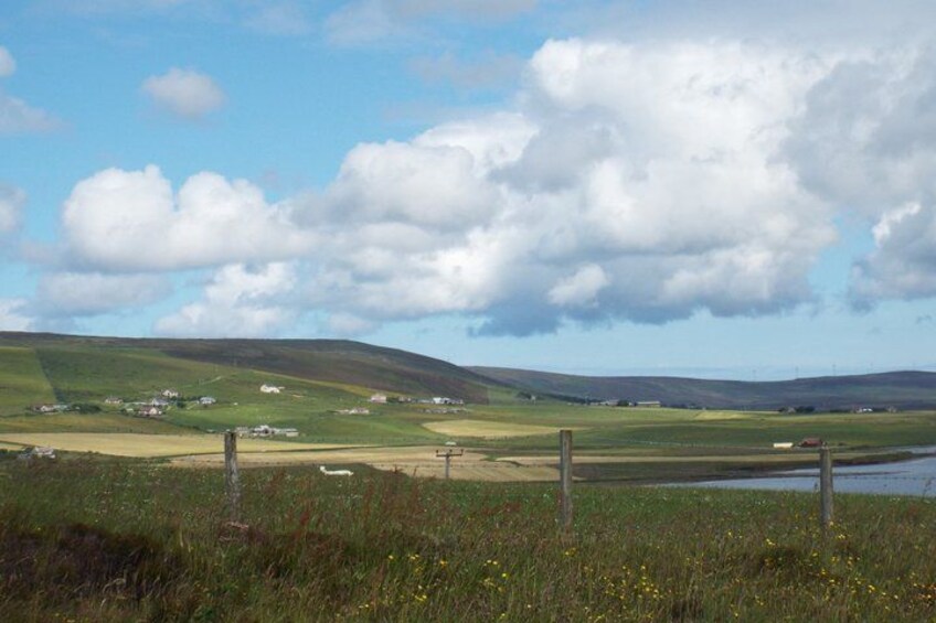 A rural landscape with rolling hills, a fence, and a small body of water. 1