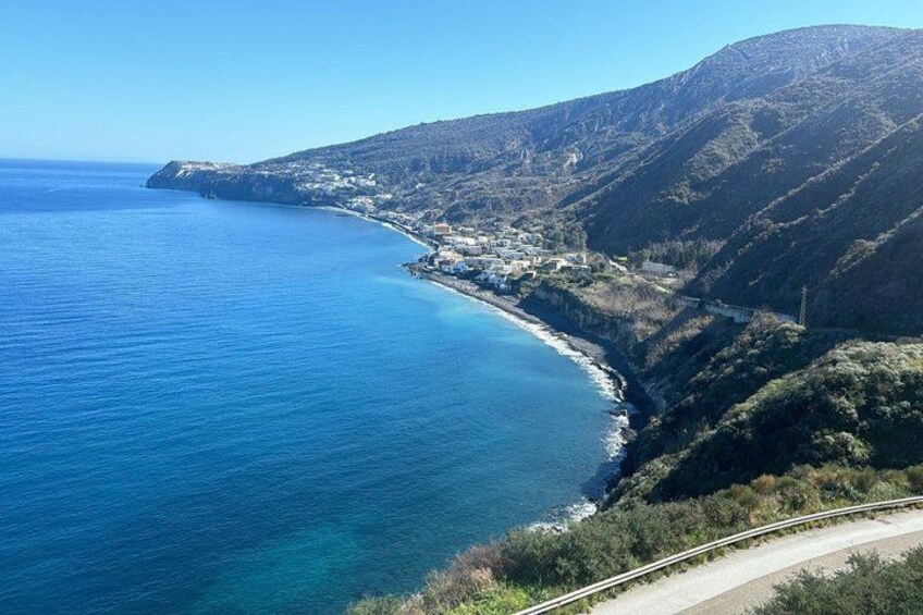 A coastal landscape with a clear blue sea, a winding road, and a hilly terrain. 5