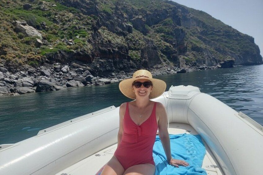 A person in a red swimsuit sitting on a boat with a blue towel, surrounded by rocky cliffs and calm water. 2