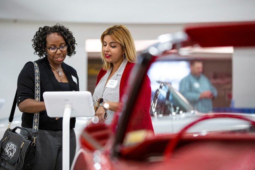 Two people examining a red sports car in a showroom. 4