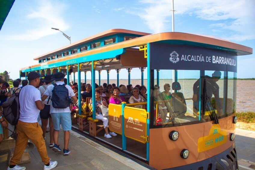 A cable car with passengers, labeled 'ALCALDÍA DE BARRANQUILLA,' at a docking station by a body of water. 4