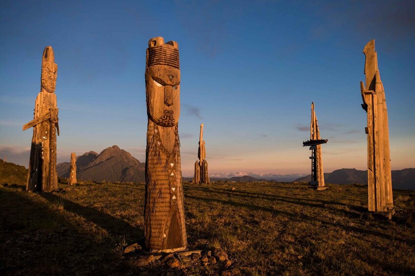 A series of ancient stone structures with carvings, set against a mountainous backdrop during sunset. 1