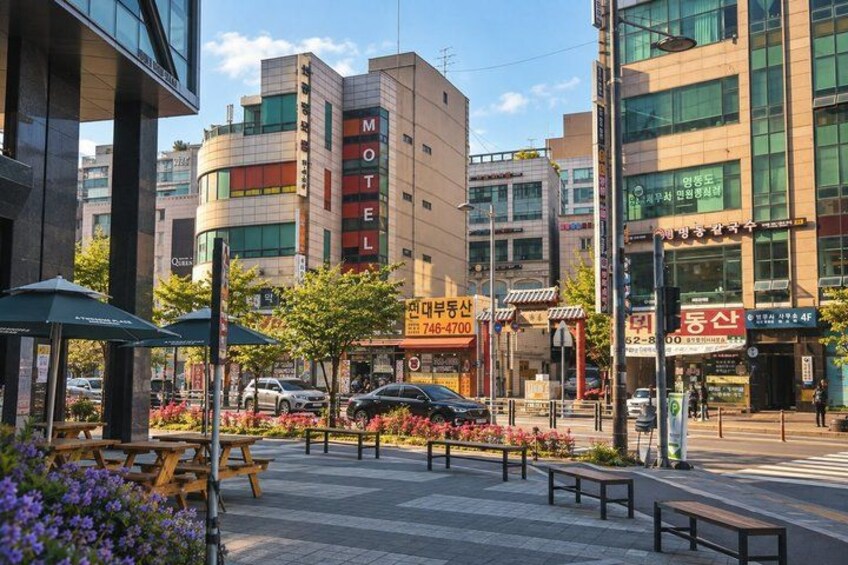 A city street with a motel, benches, and a flower bed. 3