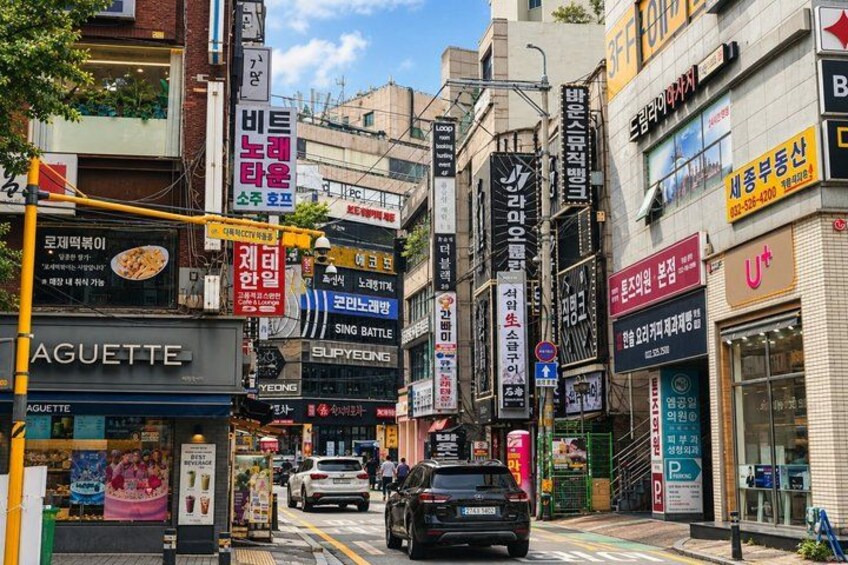 A busy urban street with various shops and signs, including a visible 'SING BATTLE' sign. 2