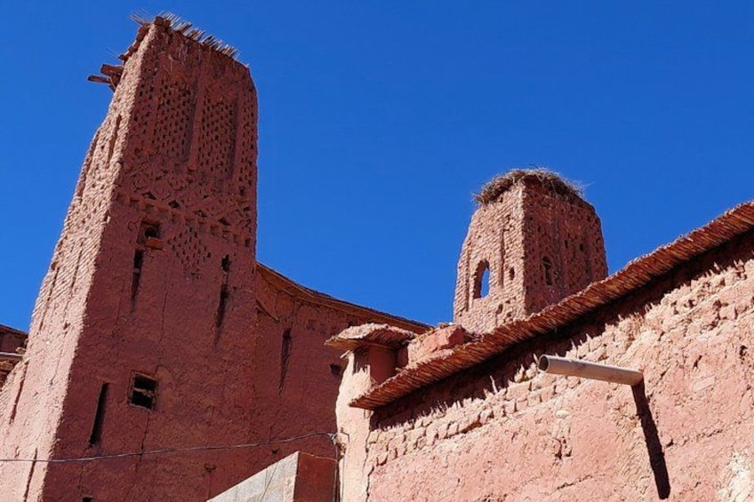 A red brick tower with a smaller tower attached to it, both with crenellations, under a clear blue sky. 2