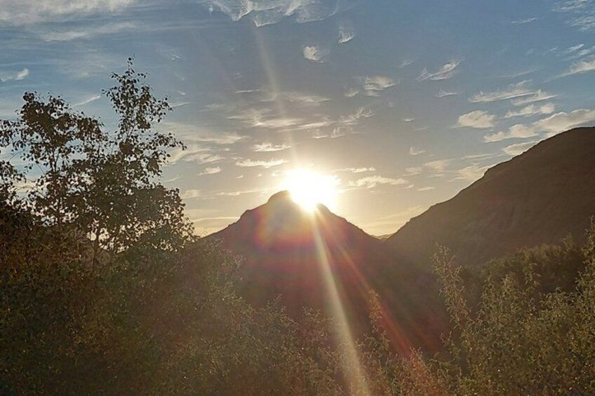 A mountain landscape with the sun setting behind it, casting rays of light. 5
