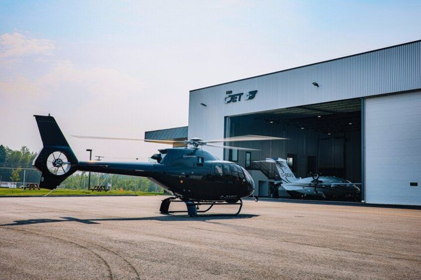 A black helicopter parked in front of a hangar. 1
