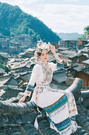 A person in traditional attire sitting on a structure with a mountainous village in the background. 2