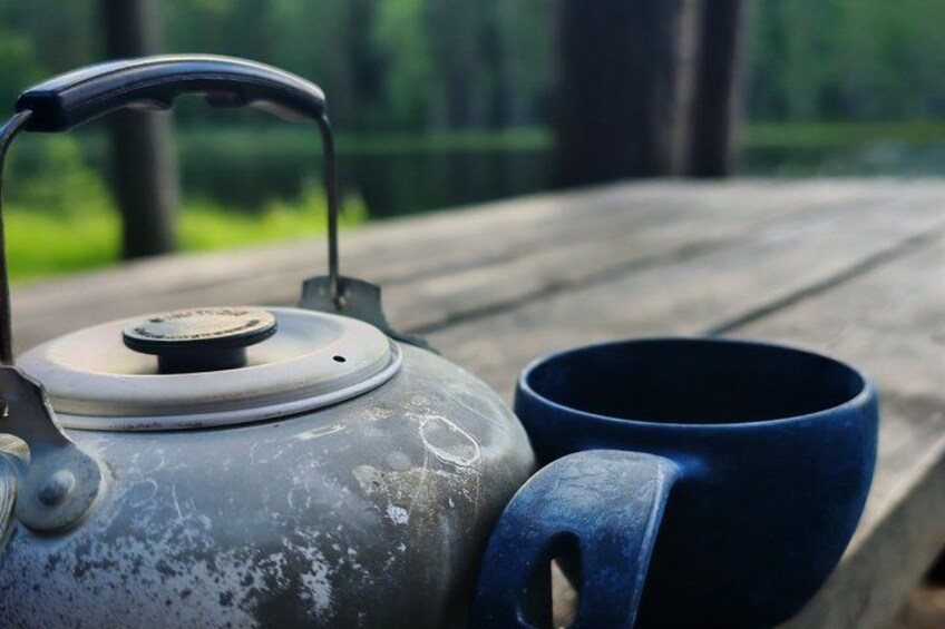 A metal kettle with a lid and a blue mug on a wooden surface. 4