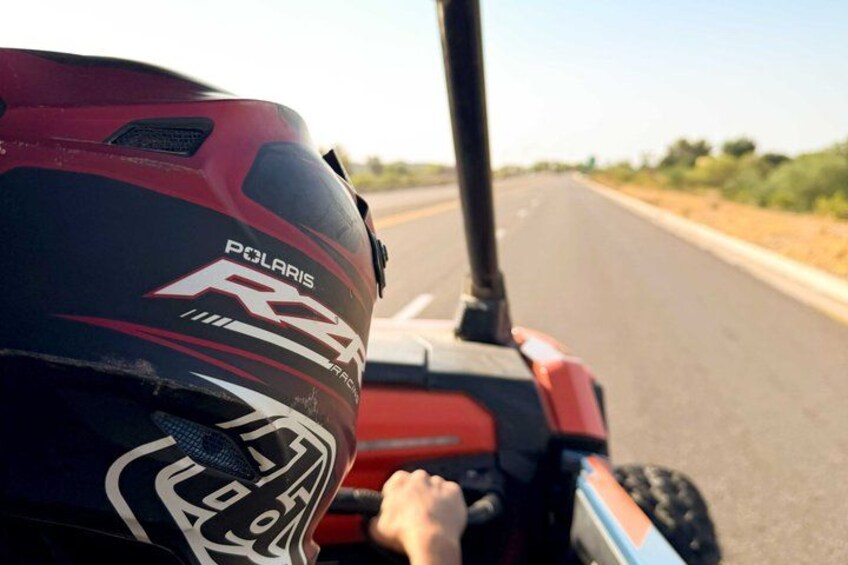 A red Polaris RZR on a road with a helmet on the seat. 3
