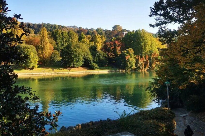 A calm lake surrounded by trees with autumn foliage, a clear sky, and a distant hill. 5