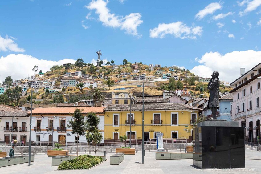 Ein Stadtplatz mit einer Statue, Gebäuden und einer Hügelkette im Hintergrund. 1