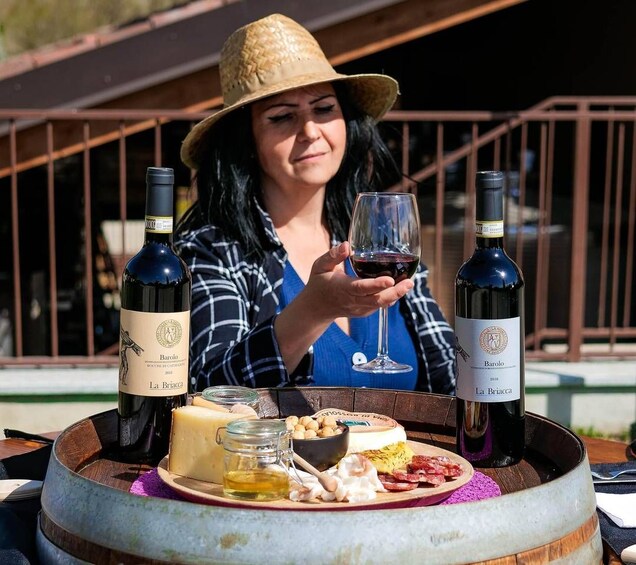Une personne tenant un verre à vin, avec deux bouteilles de vin étiquetées « La Briacca » sur une table où se trouvent du fromage, des noix et un pot de miel. 5