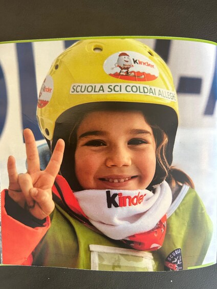 A child wearing a yellow helmet with 'Kinder' branding and a peace sign. 1