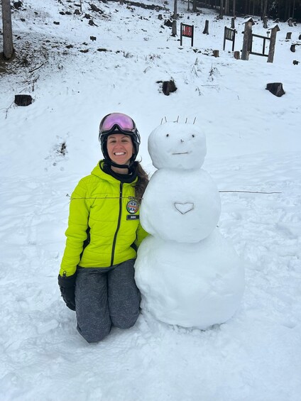 A person in a yellow jacket and helmet next to a snowman with a heart-shaped nose. 2
