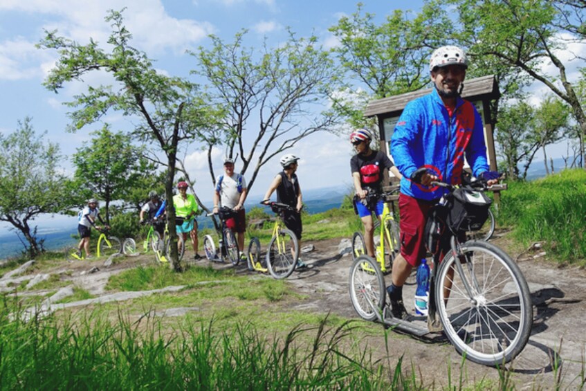 A group of cyclists on a mountain bike trail with trees and a clear sky. 3