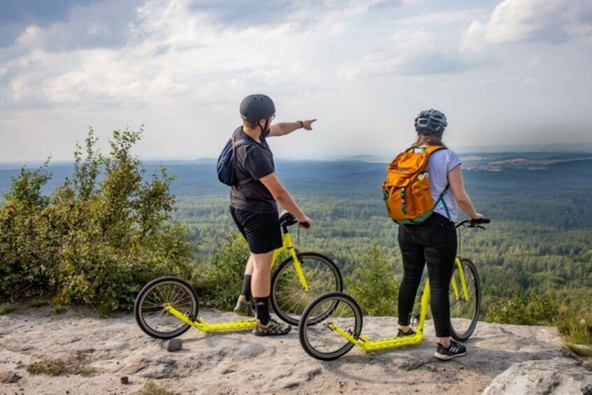 Two people on a mountain bike trail overlooking a forested valley. 1