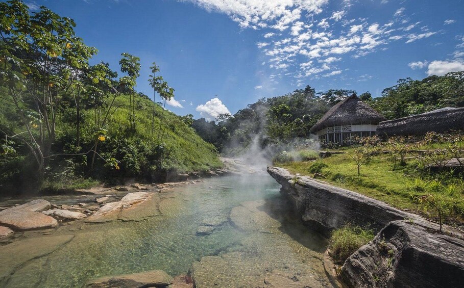 Une rivière aux eaux claires, parsemée de rochers, une hutte à toit de chaume et une végétation luxuriante. 1