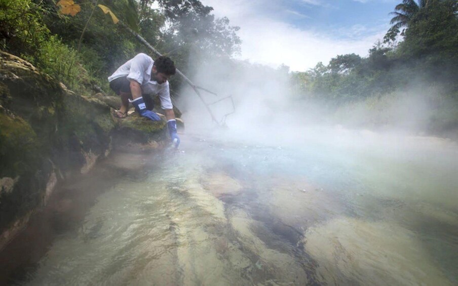 Une personne vêtue d’une chemise blanche et d’un short bleu, se tenant près d’une étendue d’eau brumeuse, entourée de verdure. 3