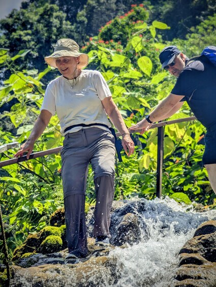 Two people crossing a small waterfall in a lush, green environment. 3