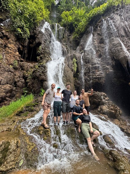 A group of people posing in front of a waterfall with lush greenery in the background. 4