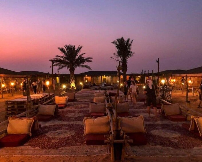 Un área de estar al aire libre con sillones, mesas, palmeras y un cielo al atardecer. 2