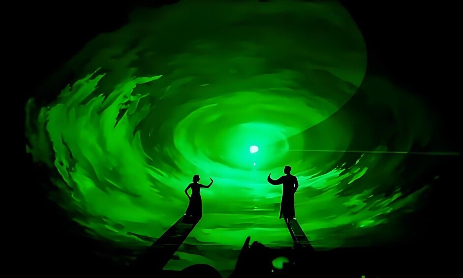 Deux silhouettes se dressent sur une plateforme, une lumière verte illuminant le centre d’un tunnel en spirale. 2