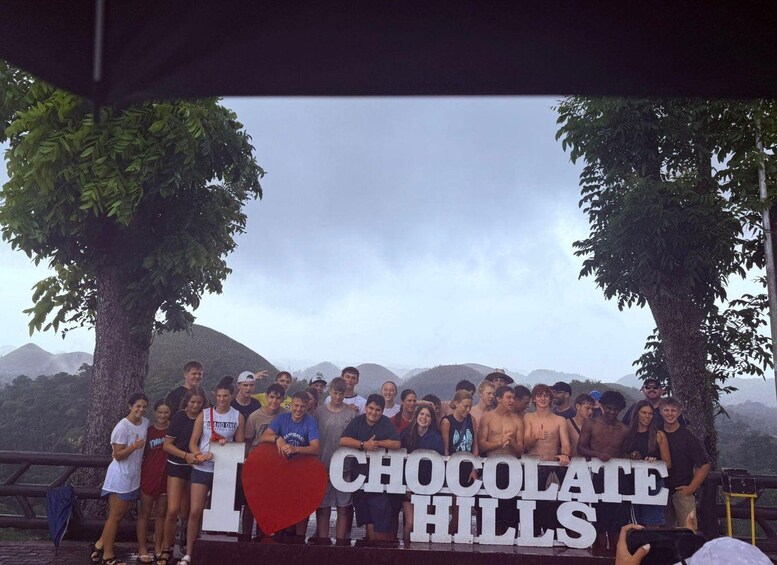 Eine Gruppe von Personen posiert vor einem Schild mit der Aufschrift 'I LOVE CHOCOLATE HILLS'. 5