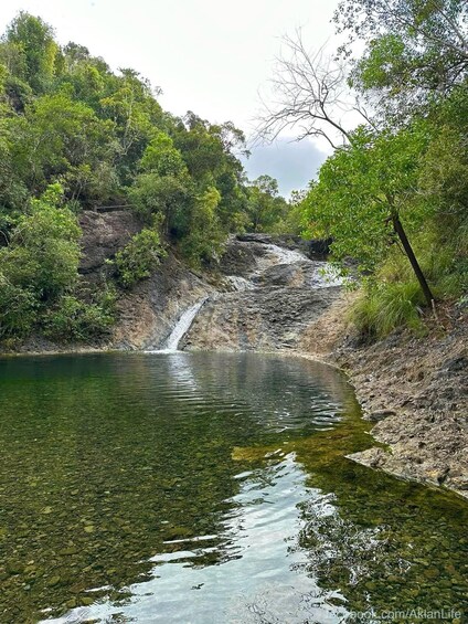 A serene lake with a waterfall, surrounded by lush greenery and rocky terrain. 3