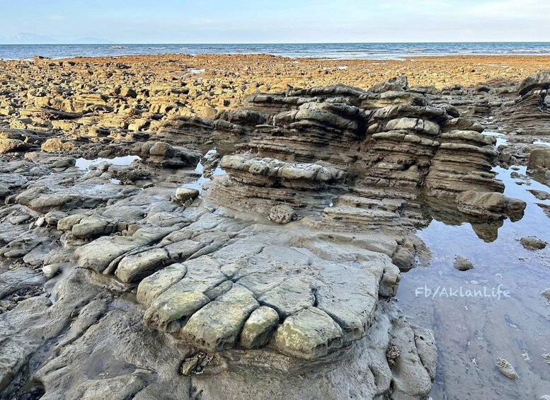 A rocky shoreline with layered sedimentary rock formations and calm sea in the background. 2