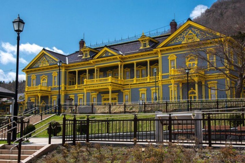 A large, yellow-painted building with a balcony and steps leading up to it. 2