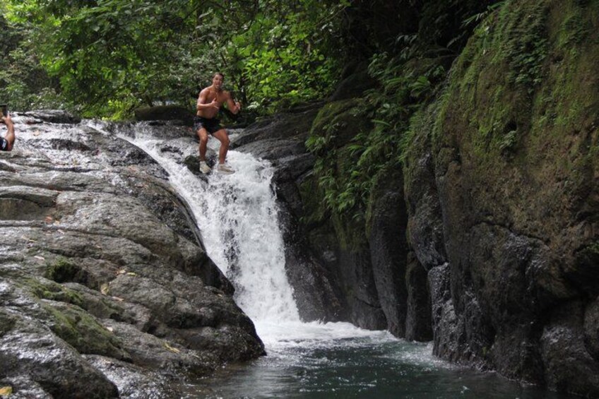A person jumping off a rocky waterfall in a forested area. 4