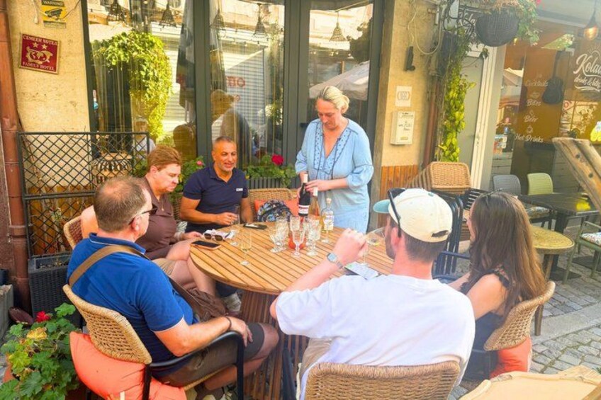 A group of people sitting at an outdoor table, engaged in conversation, with a waiter attending to them. 2