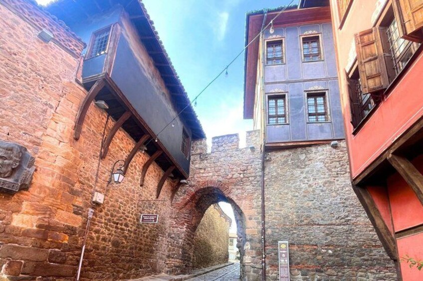 A narrow alleyway with a brick wall, a wooden door, and a stone archway. 1