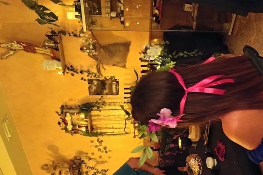 A room with a yellow carpet, a table with various items, and a person with a pink ribbon in their hair. 5