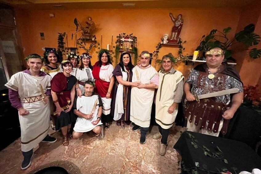 A group of people in historical costumes posing for a photo in a room with a statue and plants. 1