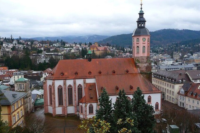 A church with a clock tower, surrounded by a town with buildings and a mountain in the background. 4