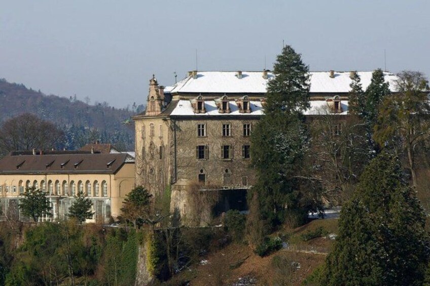 A historic building with a snow-covered roof, surrounded by trees and a hilly landscape. 2