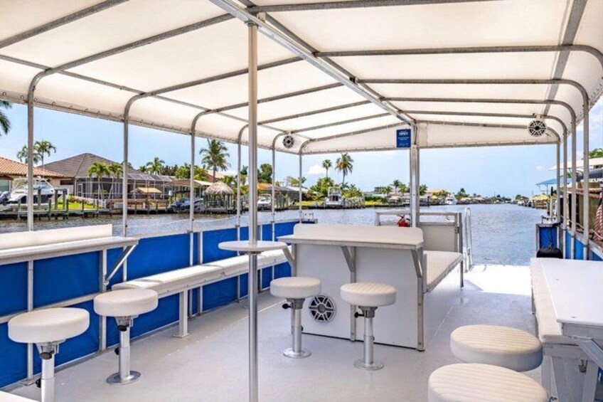 A covered deck with bar stools, a bar area, and a view of a marina with boats and palm trees. 4
