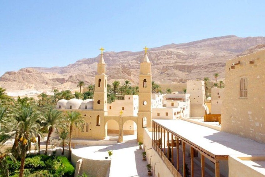 A desert landscape with a church featuring two towers and a cross on top, surrounded by palm trees and buildings. 4