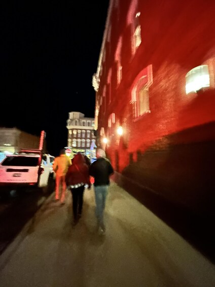 A nighttime street scene with a red building, a white car, and people walking. 2